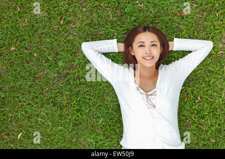 Young woman lying on the lawn with hands benind head Stock Photo