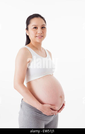 Pregnant woman smiling at the camera with hands on abdomen, Stock Photo