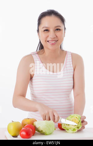 Pregnant woman cutting vegetables and smiling at the camera, Stock Photo
