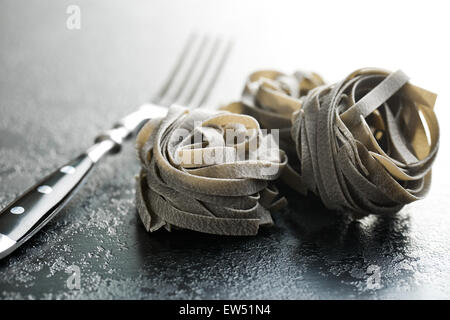 black tagliatelle pasta and fork on kitchen table Stock Photo