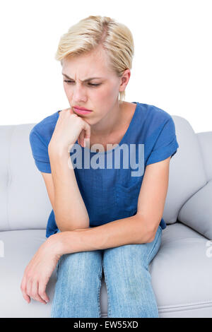 Thoughtful blonde woman sitting on the couch Stock Photo