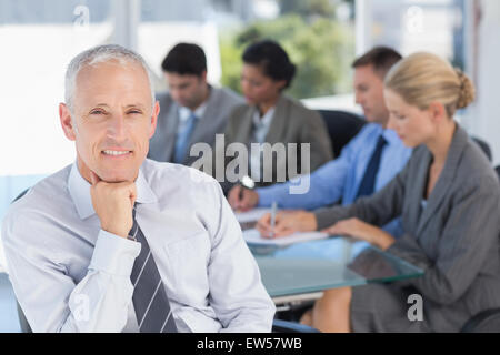 Businessman smiling at camera with colleagues behind Stock Photo