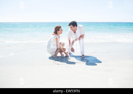 Happy couple drawing heart shape in the sand Stock Photo