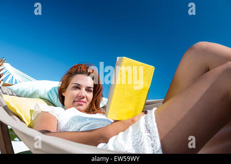 Brunette reading a book while relaxing in the hammock Stock Photo