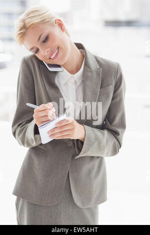 Businesswoman using her smartphone and writing notes Stock Photo