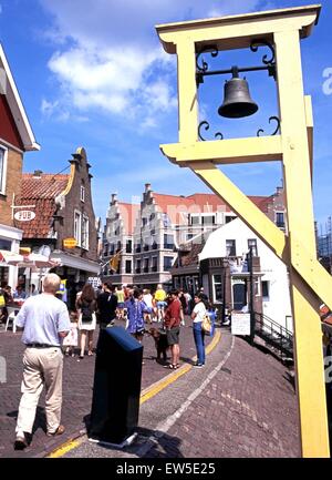 Bell on harbour wall with tourists walking along the shopping street, Volendam, Holland, Netherlands, Europe. Stock Photo