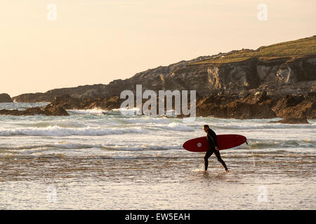 A surfer carries his surfboard as he walks into the sea at Fistral. Stock Photo