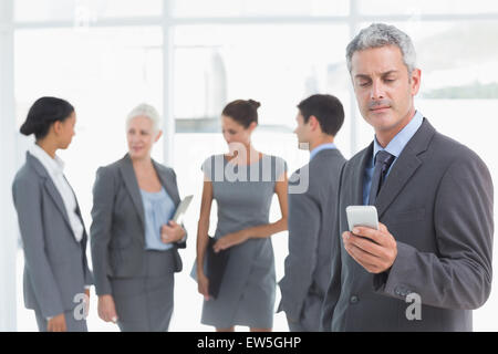 Businessman using mobile phone with colleagues behind Stock Photo