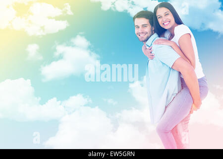 Composite image of happy casual man giving pretty girlfriend piggy back Stock Photo