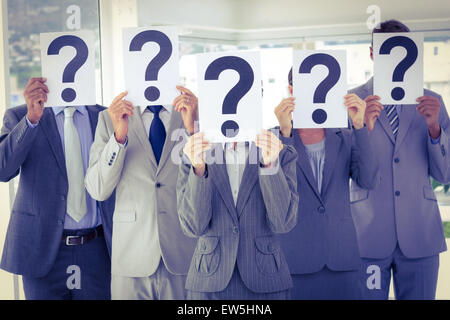 Business team holding question marks over face Stock Photo