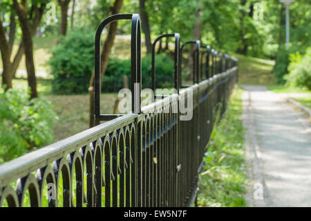 Vanishing decorative wrought iron fence in sunny park Stock Photo