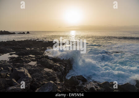 Sun setting over waves breaking on seacoast of Tenerife island, Spain Stock Photo