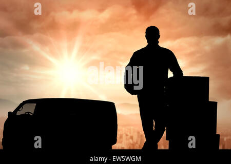 Composite image of handsome delivery man leaning on stacked cardboard boxes Stock Photo