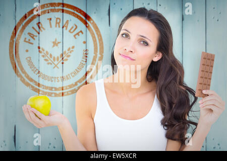 Composite image of pretty brunette deciding between apple and chocolate Stock Photo