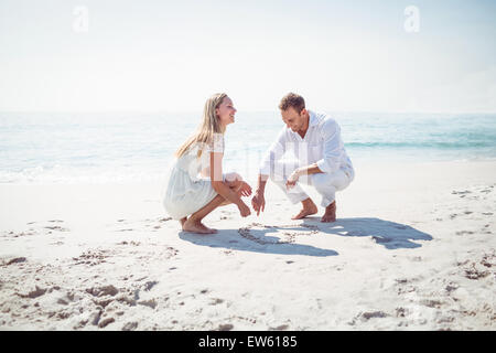 Happy couple drawing heart shape in the sand Stock Photo