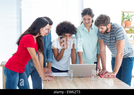 Colleagues gathered around a laptop at office Stock Photo