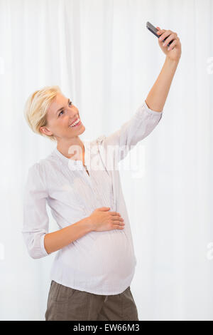 Smiling blonde pregnant woman taking a selfie Stock Photo