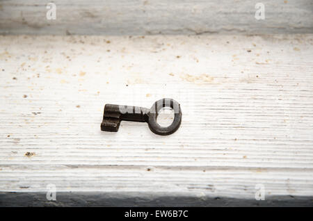 An old rusty key at a dirty white painted wooden surface Stock Photo
