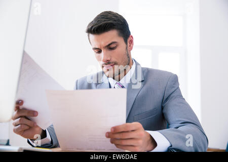 Confident businessman sitting at the table in office and reading documents Stock Photo