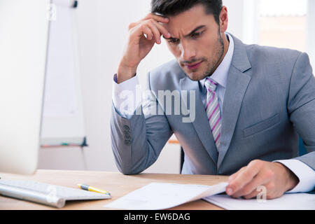 Handsome businessman sitting at the table in office and reading document Stock Photo