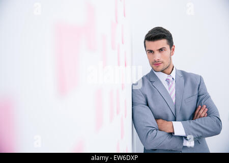 Confident businessman with arms folded leaning on the wall with stickers in office Stock Photo