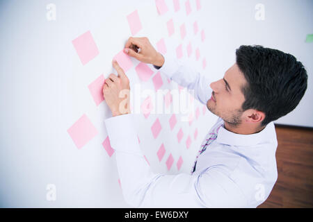 Businessman looking at sticker on wall in office Stock Photo