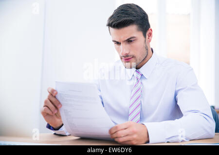 Handsome businessman sitting at the table reading document in office Stock Photo
