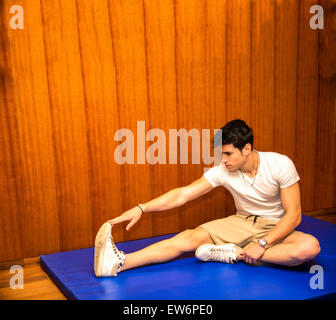Attractive young man stretching on gym mat, touching foot with hands, looking in camera Stock Photo
