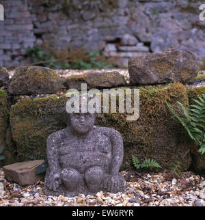 Weathered stone statue beside mossy stone wall in country garden Stock Photo