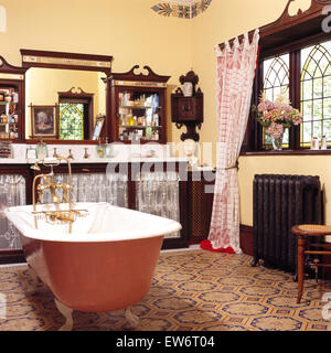 Painted roll top bath in nineties Edwardian style bathroom with patterned floor tiles and mahogany vanity unit Stock Photo