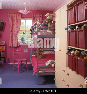 Metal bunk beds in child's bright pink nineties bedroom with plastic storage bins on built in shelves Stock Photo