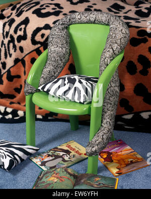 Green plastic chair draped with a fabric snake in child's nineties economy style bedroom Stock Photo