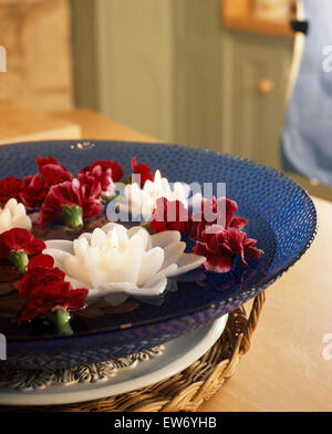 Still-Life of waterlily candles floating in a blue glass bowl with red carnations Stock Photo