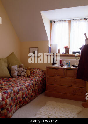 Patchwork quilt on single bed in child's attic bedroom with pine chest of drawers Stock Photo