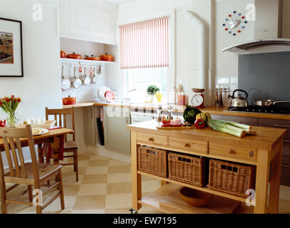 Wicker storage baskets on shelf of wooden table in center of white kitchen with wooden dining table and chairs Stock Photo