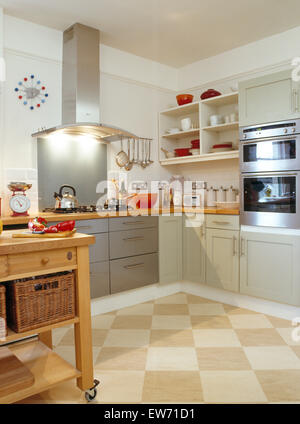 Tiled checkerboard flooring in modern kitchen with integral lighting on stainless steel extractor above hob in gray fitted unit Stock Photo