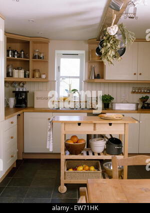 Dried herbs and pans on beam above wooden butcher's block in cottage kitchen with slate tiled floor Stock Photo