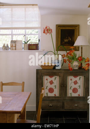 Pot of amaryllis and vase of tulips on small painted cupboard in cottage dining room Stock Photo