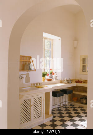 Arched doorway to white Moroccan kitchen with black+white checkerboard tiled floor Stock Photo