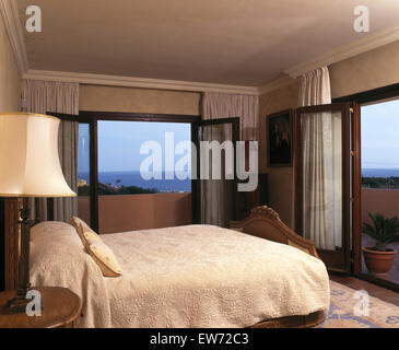 White quilt on bed in Spanish coastal bedroom with a view of the sea through open patio doors Stock Photo