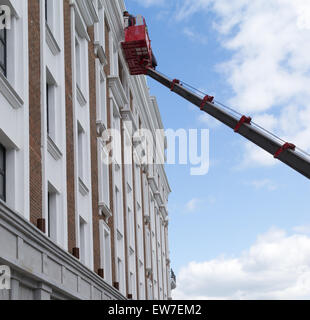 Workers working on a building facade using a red hydraulic lift Stock Photo