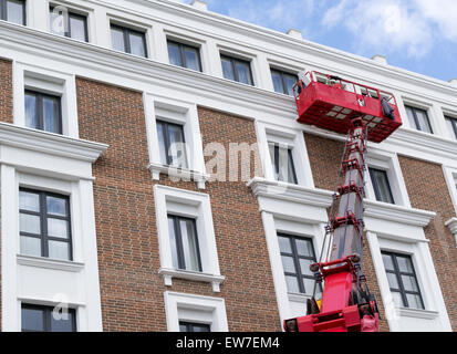 Workers working on a building facade using a red hydraulic lift Stock Photo