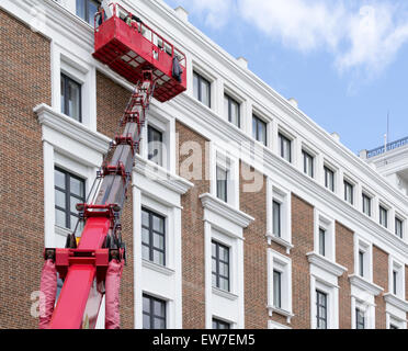 Workers working on a building facade using a red hydraulic lift Stock Photo