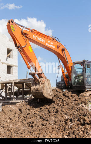 Orange digger excavates soil in preparation for new apartments for young families in Ufa city Bashkortostan Russia in June 2015 Stock Photo