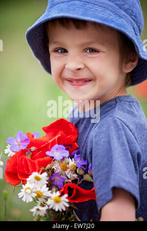 Cute kid boy with poppy flowers and other wild flowers in poppy field on warm summer day, nice soft evening light Stock Photo