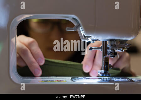 A woman using an electric sewing machine in a dark environment. Stock Photo