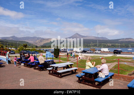 People sitting outside Little Rock cafe with a view to Goat Fell mountain across Brodick Bay on a sunny day. Brodick Isle of Arran Scotland UK Stock Photo