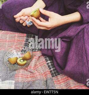 Close-up of a woman sitting on a rug eating a kiwi fruit Stock Photo