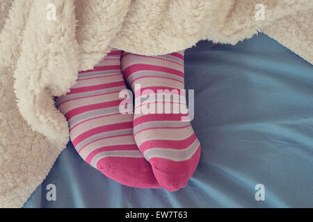 Woman's feet in pink socks sticking out from under a blanket Stock Photo