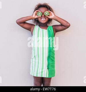 Smiling girl in green dress holding kiwi fruit in front of her eyes Stock Photo